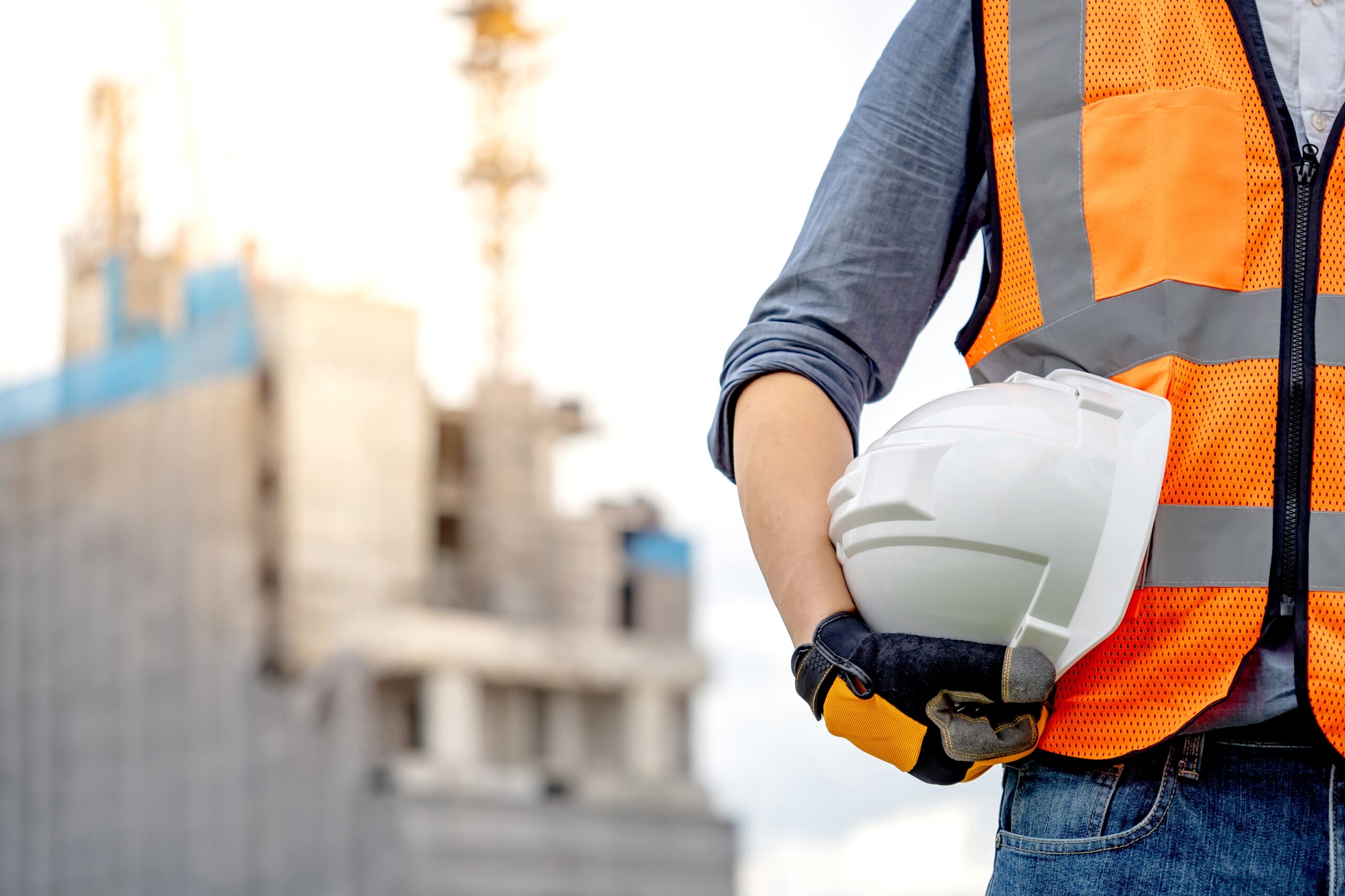 Construction worker man with hard hate, reflective orange vest and protective gloves standing at construction site